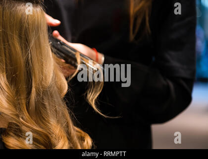 Close up de jolie jeune femme obtient ses cheveux égalisés en instituts de beauté. La coiffure est peignant ses cheveux et la tenue d'un fer à repasser. Lisser les cheveux Banque D'Images