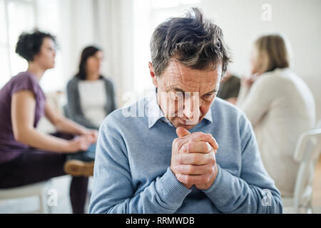 Un portrait de l'homme déprimé senior pendant la thérapie de groupe, à la recherche vers le bas. Banque D'Images