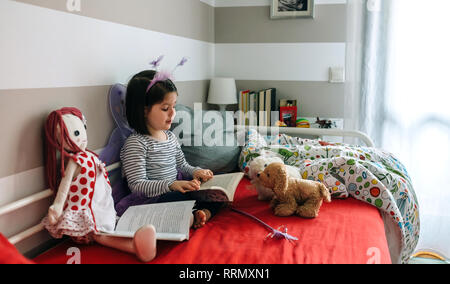 Déguisée de fille lire un livre à ses jouets Banque D'Images