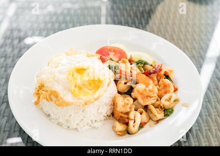 Fruits de mer frits épicés avec des feuilles de basilic sur le riz au jasmin et œuf frit Banque D'Images