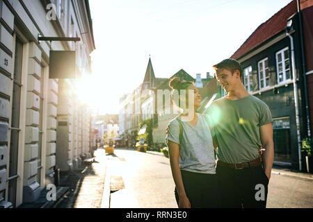 Laughing young couple marcher ensemble le long d'un trottoir de la ville Banque D'Images