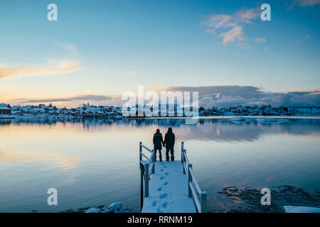 Couple au bord de quai enneigé surplombant le Waterfront Village, Reine, îles Lofoten, Norvège Banque D'Images