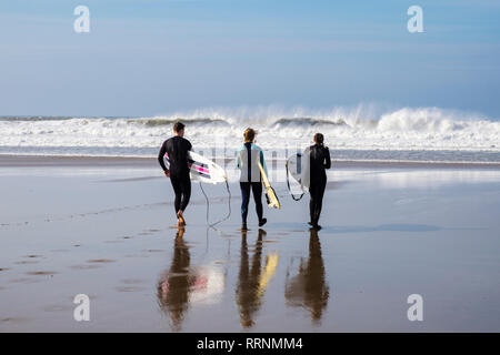Trois surfeurs avec des conseils d'administration reflètent dans le sable humide en tête à la surf sur la plage de Woolacombe, Devon, Angleterre, Royaume-Uni, Angleterre Banque D'Images
