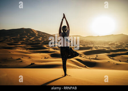 Serene woman standing in yoga posture de l'arbre sous le soleil de désert de sable, Sahara, Maroc Banque D'Images