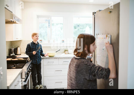 Frère et soeur la cuisson et de l'écriture sur le calendrier dans la cuisine Banque D'Images