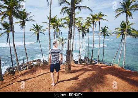 Jeune homme à marcher entre les palmiers contre la mer. Littoral au Sri Lanka. Banque D'Images