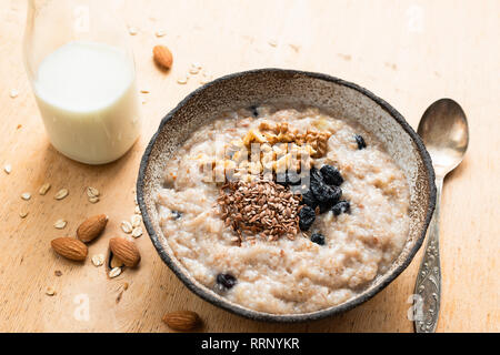 L'avoine dans un bol de porridge petit-déjeuner sur la table en bois. Bouillie d'avoine et aux raisins secs, noix et linseeds préparé avec le lait d'amande Banque D'Images