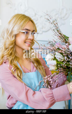 Beautiful smiling female florist in apron holding bouquet in flower shop Banque D'Images