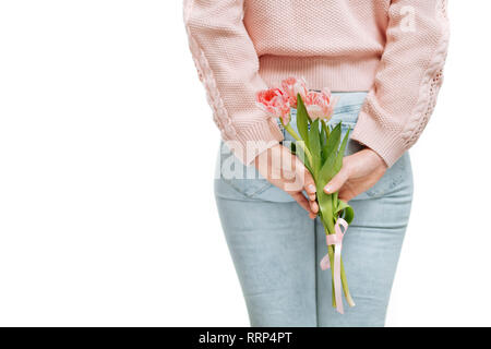 Jeune femme tenant de tulipes roses derrière son dos sur un fond blanc. Banque D'Images