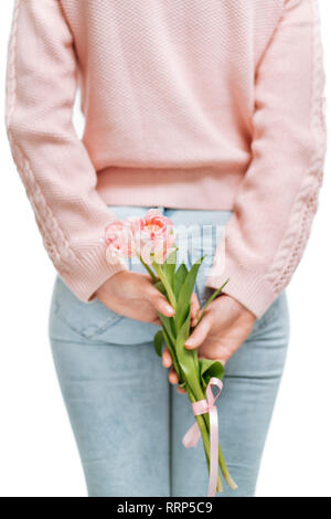 Jeune femme tenant de tulipes roses derrière son dos sur un fond blanc. Banque D'Images