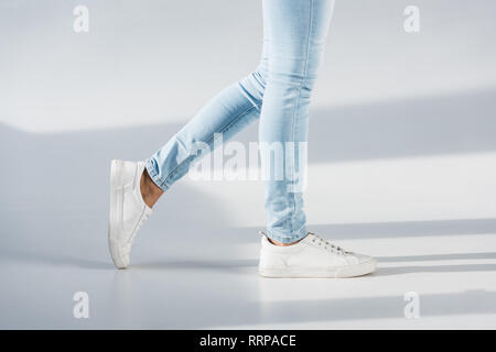 Vue partielle de la femme en bleu jeans et chaussures blanches sur fond gris Banque D'Images