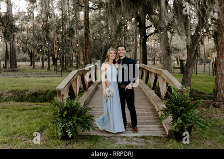 Belle robe de demoiselle d'honneur la Femme en bleu et le Bouquet avec sa date au cours d'une célébration de mariage à l'extérieur de l'événement dans les bois en tenant l'orifice Couple Banque D'Images