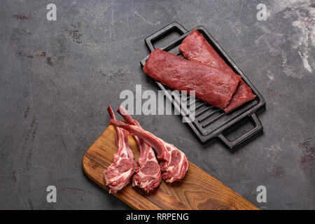 Matières premières de viande de mouton fraîche sur l'os Chesno épices et de romarin sur un fond noir. la cuisson des aliments Banque D'Images