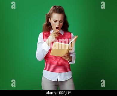 Surpris en apprenant moderne femme jeans gris et rose T-shirt de la lecture d'un livre jaune contre un arrière-plan vert. Banque D'Images