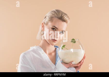 Belle jeune fille tenant un poisson bol avec du sable et des petites plantes vertes, isolé sur l'environnement, concept d'économie beige Banque D'Images