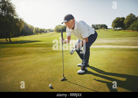 Sporty man accroupi sur une planification écologique son putt tout en profitant d'une partie de golf sur une journée ensoleillée Banque D'Images