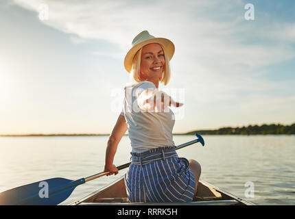 Jeune femme à l'arrière par-dessus son épaule et sa main tout en pagayant un canoë sur un lac pittoresque sous le soleil d'après-midi d'été Banque D'Images