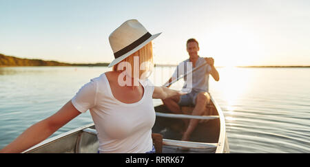 Souriante jeune femme qui remonte à son petit ami tout en pagayant un canot ensemble sur un lac sur une fin de l'après-midi d'été Banque D'Images