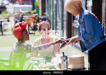 Jeune femme serveuse payer avec carte de crédit au café avec terrasse ensoleillée Banque D'Images