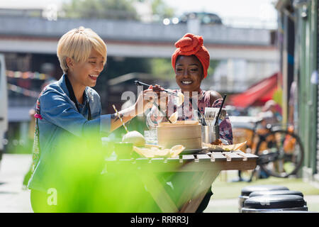 Heureux les jeunes femmes friends enjoying dim sum déjeuner au café avec terrasse ensoleillée Banque D'Images