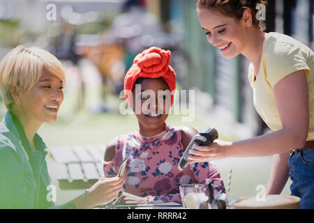 Jeune femme serveuse payer avec carte de crédit au café avec terrasse ensoleillée Banque D'Images