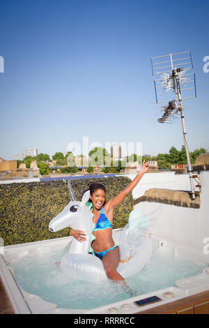 Ludique et insouciante Portrait young woman in bikini sur Pegasus gonflable à sunny bain à remous sur le toit Banque D'Images