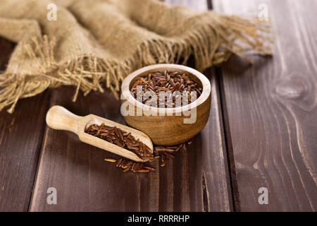 Beaucoup de riz rouge cru entier tissu du jute et d'un scoop avec bol en bois sur bois marron foncé Banque D'Images