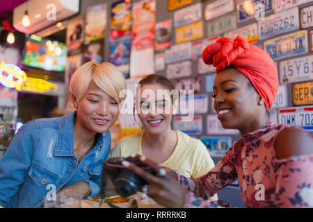 Les jeunes femmes des amis à l'aide de caméra numérique en bar Banque D'Images