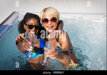 Portrait de jeunes femmes exubérantes friends drinking champagne in sunny bain à remous Banque D'Images