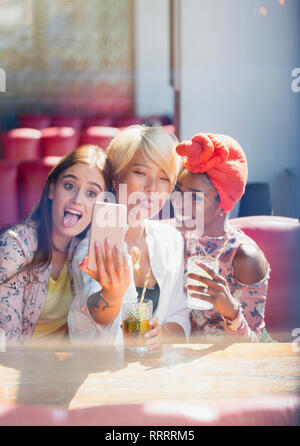 Silly, ludique les jeunes femmes friends avec selfies camera phone in cafe Banque D'Images