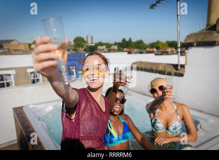 Portrait confiant, insouciant des jeunes femmes friends drinking champagne in sunny bain à remous sur le toit Banque D'Images