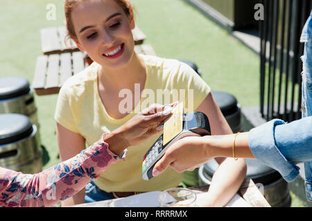 Jeune femme serveuse avec carte à puce au café avec terrasse ensoleillée Banque D'Images