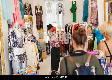 Les jeunes femmes amis avec camera phone shopping in clothing store Banque D'Images