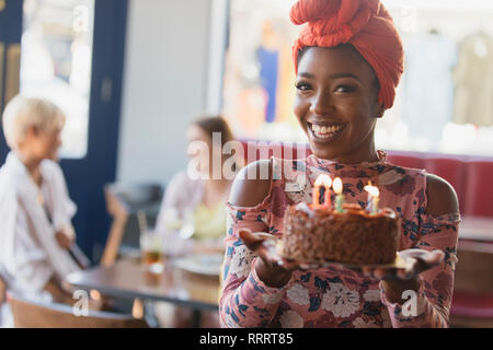 Portrait souriant, confiant Jeune femme tenant le gâteau d'anniversaire avec des bougies Banque D'Images