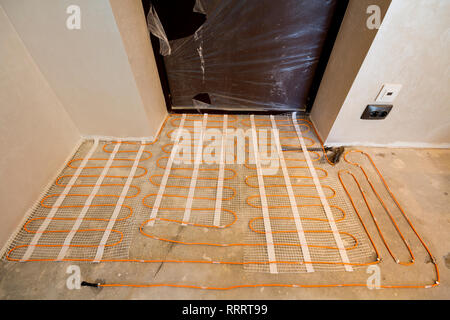 Chauffage électrique fil rouge du système installé sur le sol en ciment dans les petites nouvelles unfinished room avec plâtre des murs. La rénovation et la construction, mod Banque D'Images