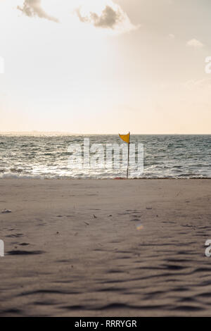 Un drapeau d'avertissement jaune indiquant des conditions défavorables sur une plage de sable blanc. Banque D'Images