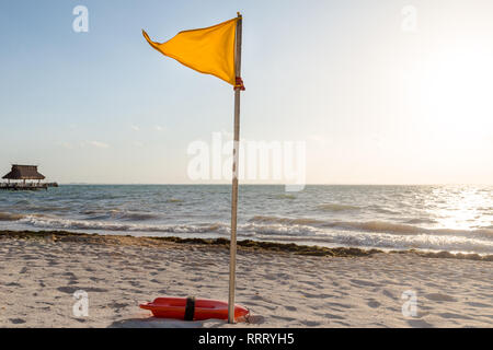 Un drapeau d'avertissement jaune indiquant des conditions défavorables sur une plage de sable blanc. Banque D'Images