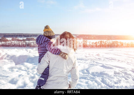 Maman avec son fils dans ses bras afin de l'arrière à l'hiver dans la ville. Les soins et l'appui d'un petit enfant à l'air libre. Dans le contexte de Banque D'Images