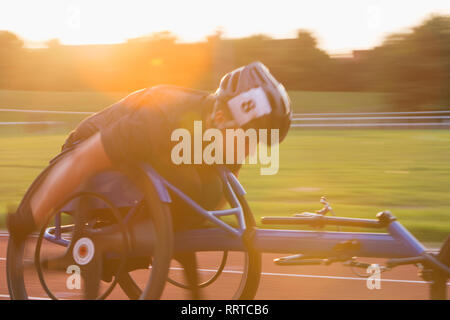 Jeune femme déterminée athlète paraplégique en accélérant le long de la piste en course en fauteuil roulant de sport Banque D'Images