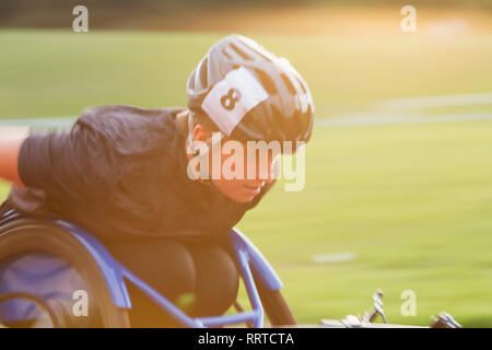 Jeune femme déterminée athlète paraplégique en accélérant le long de la piste en course en fauteuil roulant de sport Banque D'Images