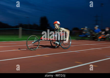 Teenage athlète paraplégique en accélérant le long de la piste en course en fauteuil roulant de sport Banque D'Images