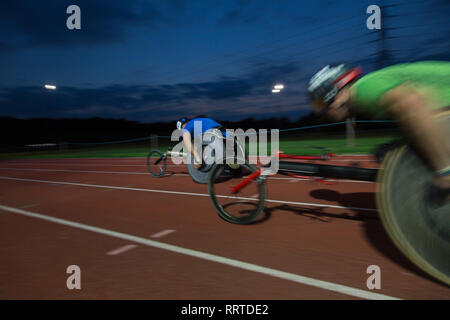 Les athlètes paraplégiques en accélérant le long de la voie des sports en fauteuil roulant de nuit course Banque D'Images