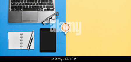 Vue de dessus de table de bureau espace de travail avec ordinateur portable, tablette, ordinateur portable blanc et café chaud crémeux verre sur fond bleu, jaune coloré table Flatlay Banque D'Images