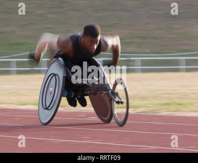 Déterminé jeune mâle athlète paraplégique en accélérant le long de la piste de course en fauteuil roulant au cours de sport Banque D'Images