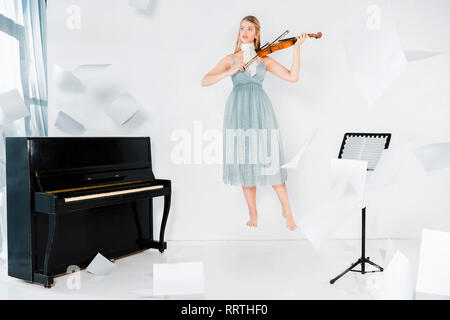 Robe fille en bleu flottant au violon près de piano avec des feuilles de papier dans l'air Banque D'Images