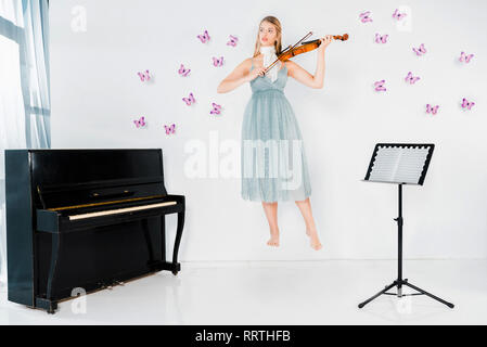 Robe fille en bleu flottant au violon près de piano sur fond blanc avec des papillons Banque D'Images