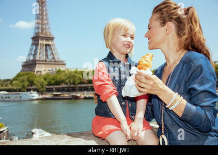 Mère et fille élégante heureux touristes avec un croissant près du parapet sur le quai de la Seine avec vue sur Tour Eiffel à Paris, Fra Banque D'Images