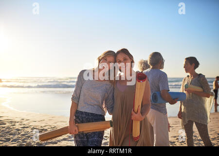 Heureux Portrait mère et fille avec un tapis de yoga sur la plage ensoleillée au cours de yoga retreat Banque D'Images