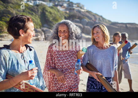 Les femmes amis avec tapis de yoga en conversation sur la plage ensoleillée au cours de yoga retreat Banque D'Images