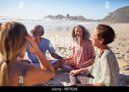 Amis assis en cercle sur la plage ensoleillée au cours de yoga retreat Banque D'Images